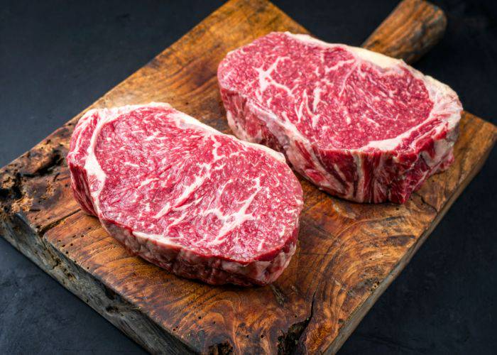 Two thick slabs of wagyu beef on a dark wooden chopping board.